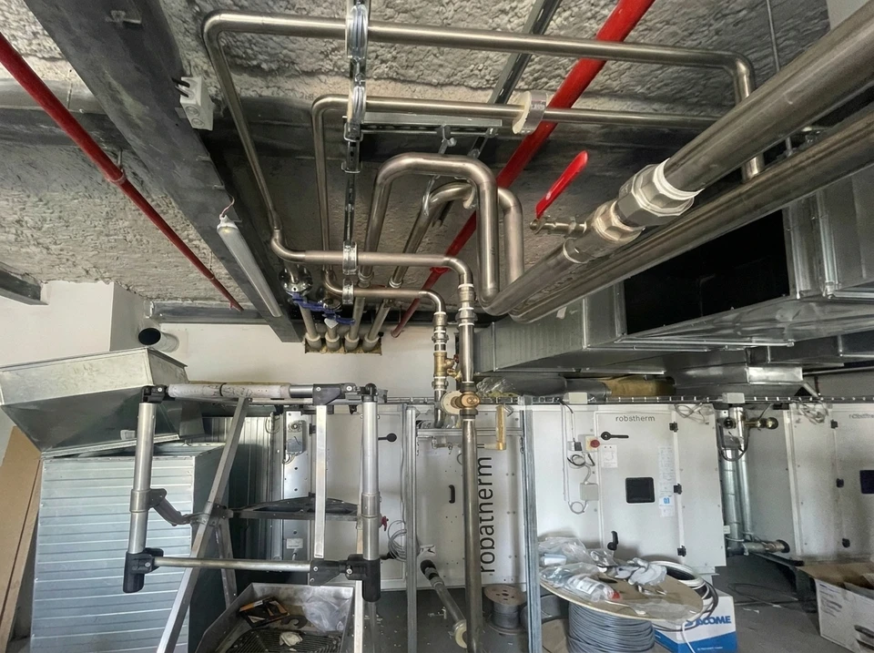 Installation technique en local technique : réseau de tuyauteries inox et cuivre, collecteur de distribution, vannes à boisseau sphérique, centrale de traitement d'air **robstherm** avec raccordements hydrauliques