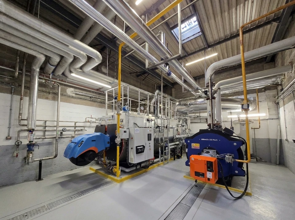 Salle de chaufferie industrielle avec deux chaudières à gaz de grande capacité, équipées de brûleurs (bleu et orange)